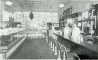 Black and white photo of an old-timey convivence store with two people behind the counter