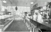 Black and white photo of an old-timey convivence store with two people behind the counter
