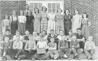 older students and teachers stand in the back while young kids sit in front