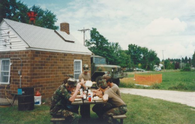 six soldiers eating at a picnic table on break from working on the house