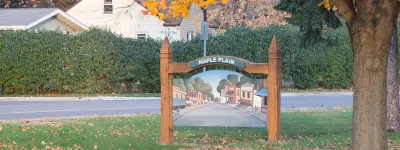Maple Plain sign on a lawn with hedges, a house, and a tree